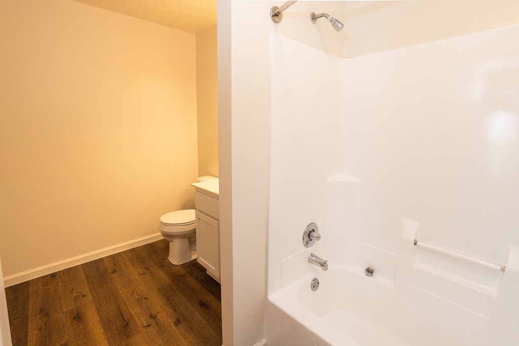 A white bathtub with a shower head and a toilet in a bathroom.