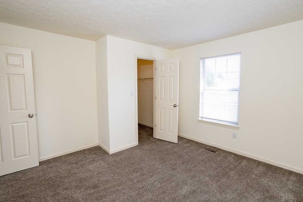 A room with a carpeted floor, two doors, and a window.