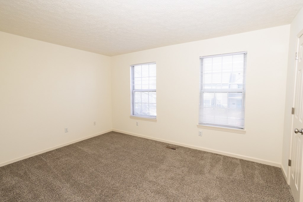 A room with carpeted floor and two windows.