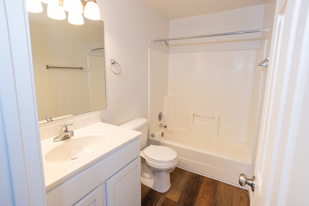 A white bathroom with a toilet, sink, mirror, and shower.