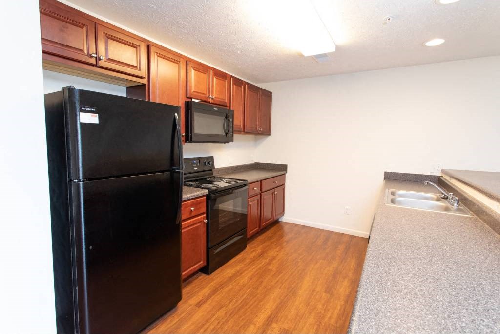 A black refrigerator is in a kitchen with wooden cabinets and a microwave.
