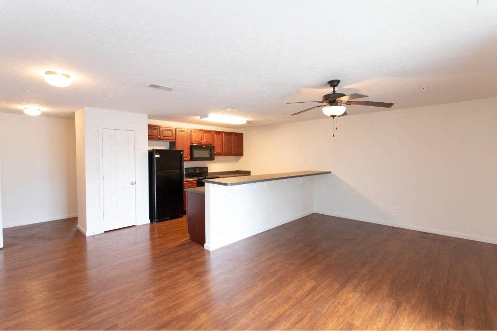 A room with a ceiling fan and a kitchenette.