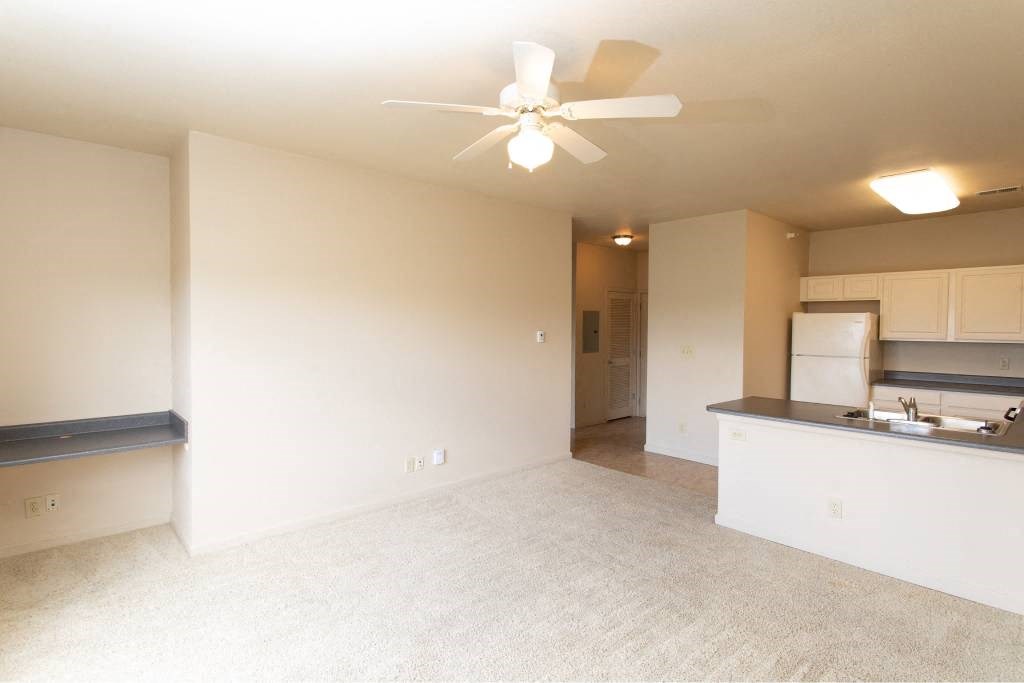 A room with a ceiling fan and a kitchenette.