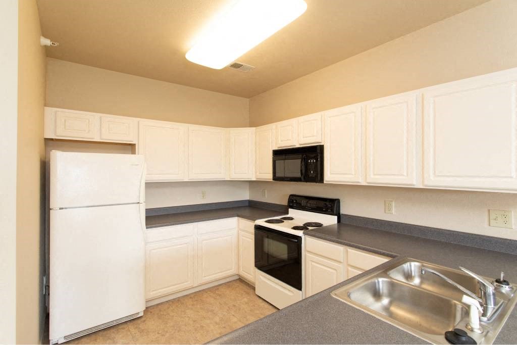 A kitchen with white cabinets and a black microwave above the stove.