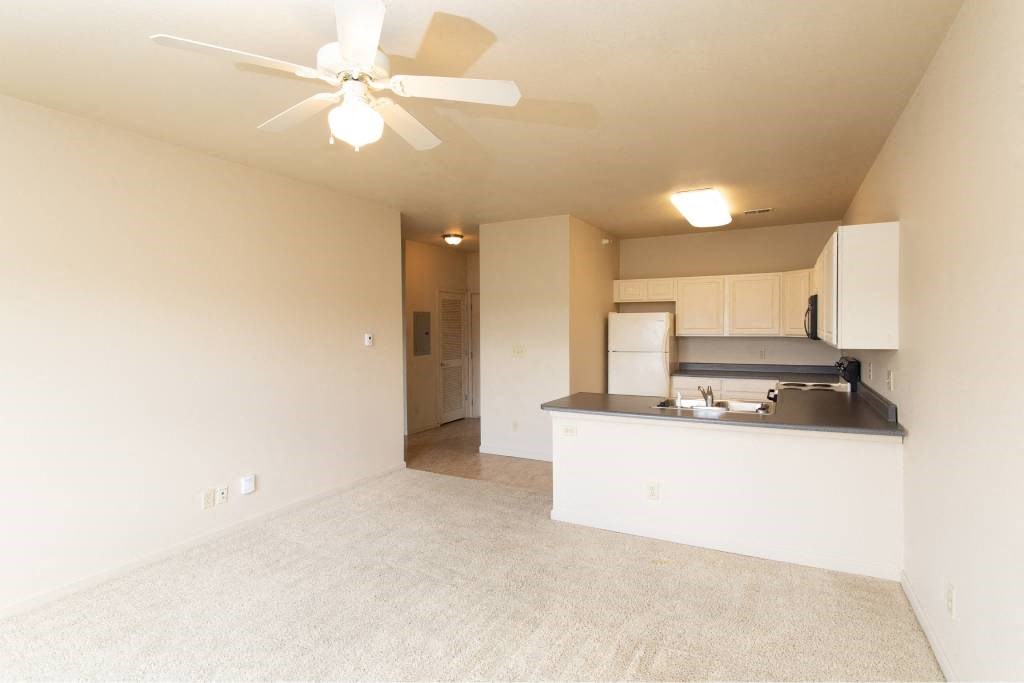 A room with a ceiling fan and a kitchenette.