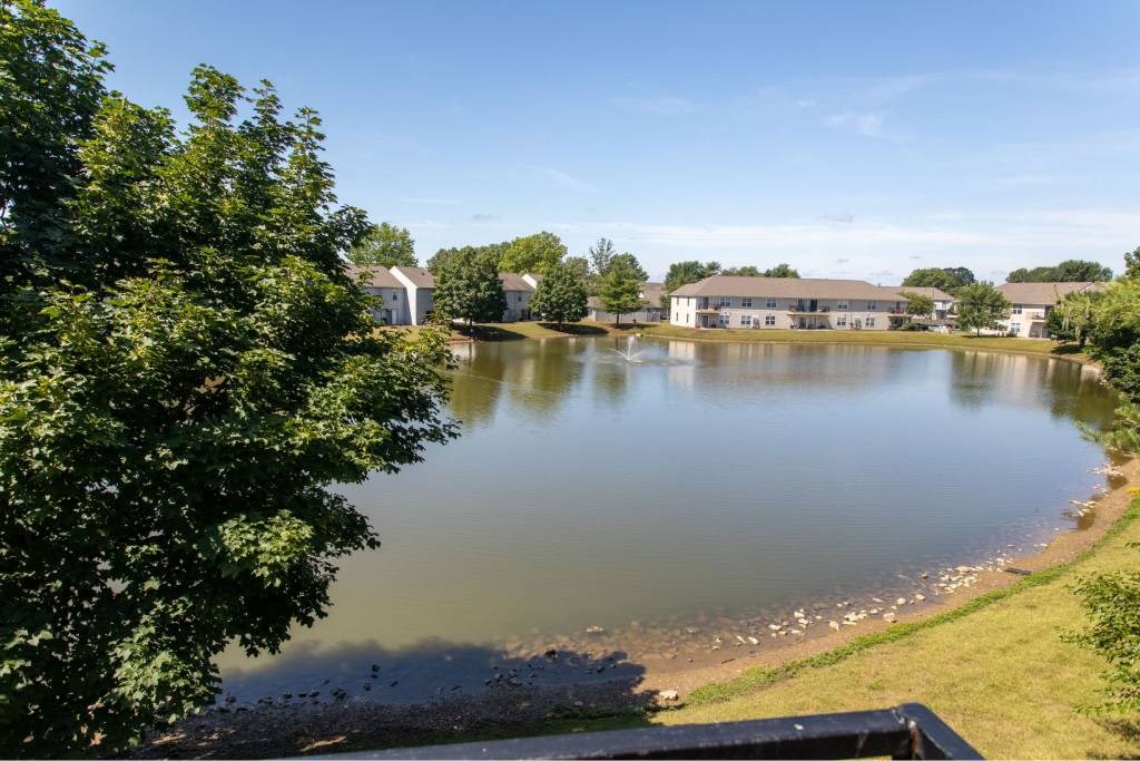A serene lake surrounded by lush greenery and a building in the distance under a clear blue sky.