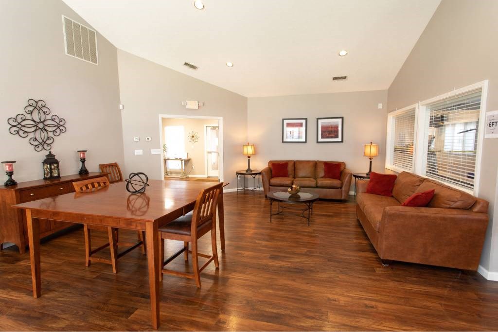 A living room with a brown couch, a wooden table and chairs, and a decorative wall hanging.