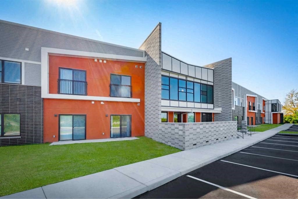 A modern building with a red and grey exterior and a parking lot in front.