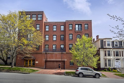 A grey car is parked in front of a red brick building.