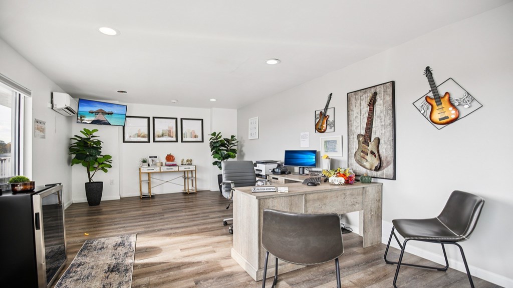A room with a desk, chairs, and guitars on the wall.