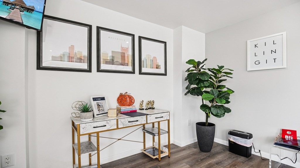 A room with a desk, chair, potted plant, and pictures on the wall.