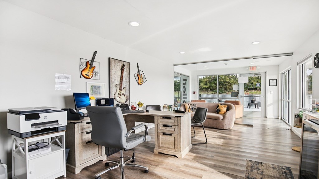 A room with a desk, chairs, and guitars hanging on the wall.