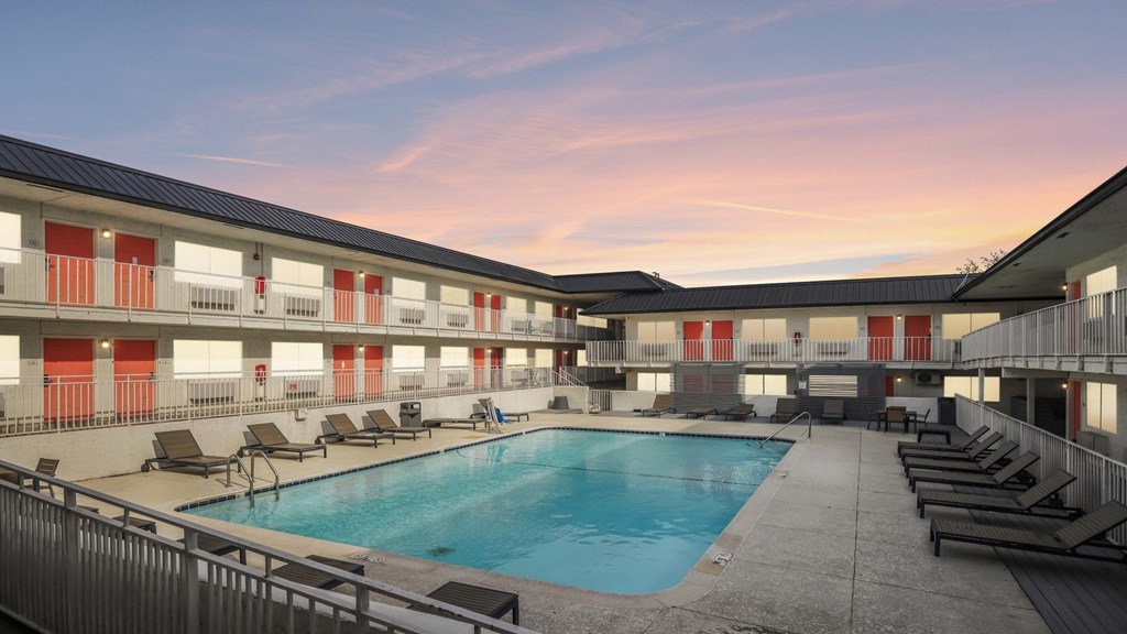 A swimming pool is surrounded by sun loungers in a courtyard.