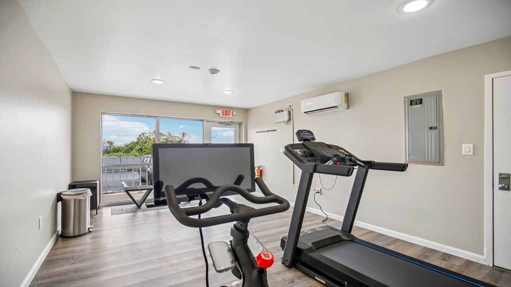 A treadmill is in a room with a TV and a window.