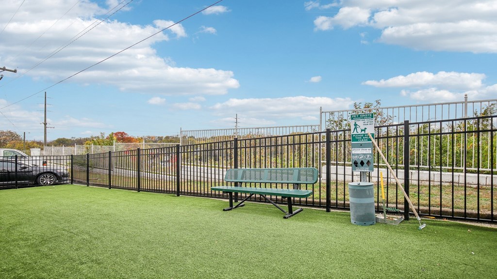 A park with a green bench and a trash can.
