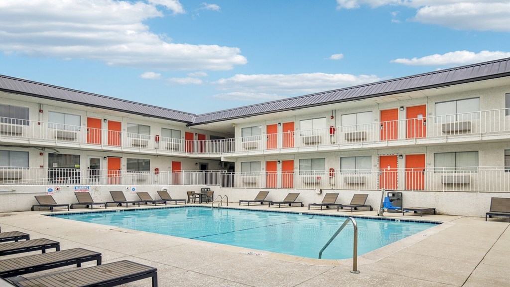 A swimming pool is surrounded by lounge chairs in front of apartment buildings.