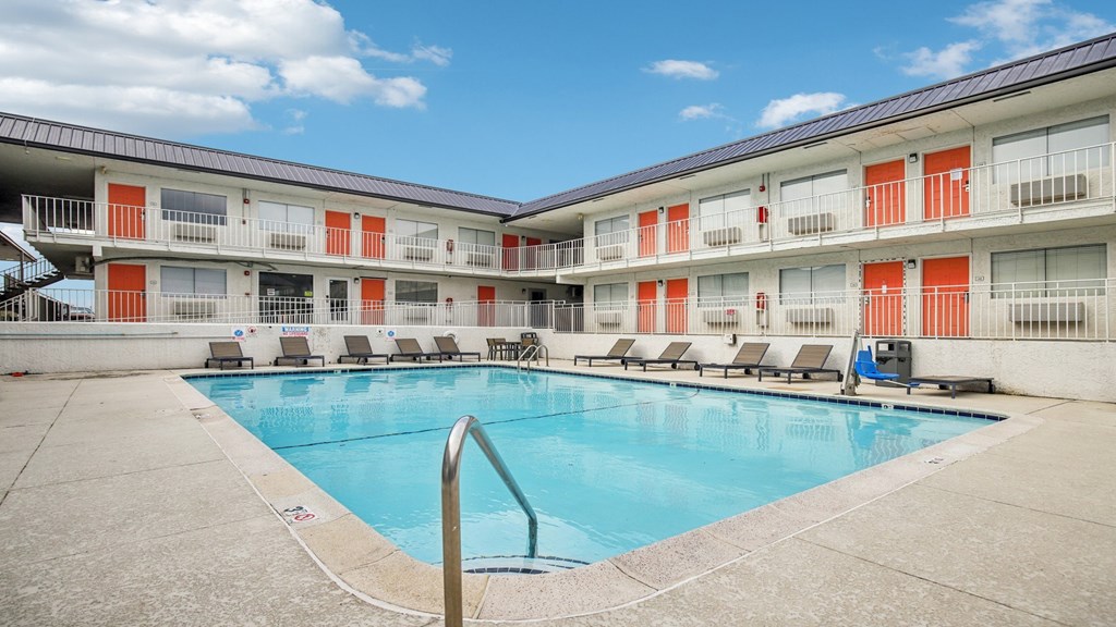 A swimming pool is surrounded by sun loungers in a sunny courtyard.