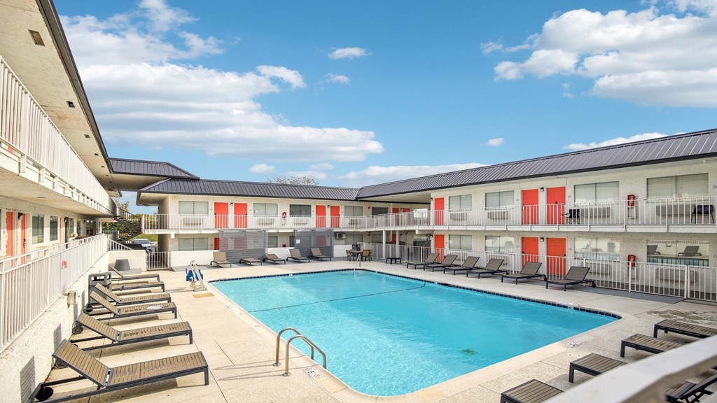 A swimming pool surrounded by sun loungers and apartment buildings.