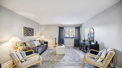 A living room with a grey sofa, two chairs, a rug, and a guitar on the wall.