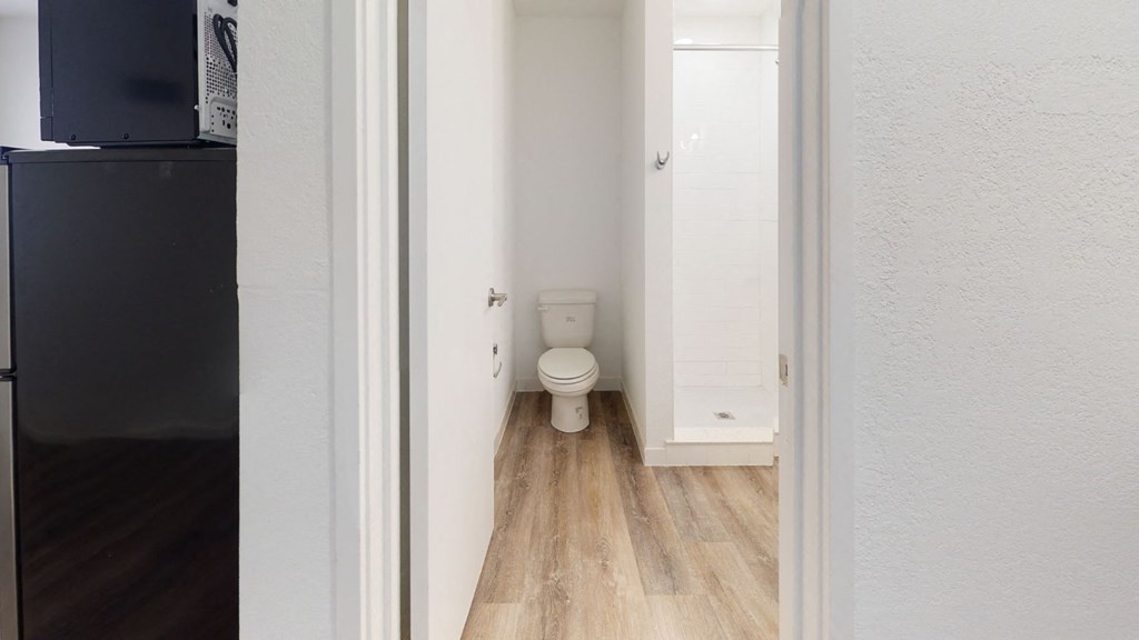A white toilet in a narrow hallway with wood flooring.