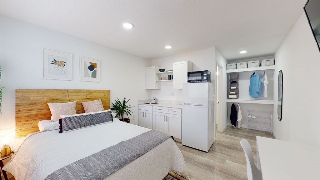 A bedroom with a bed, a potted plant, and a kitchenette.