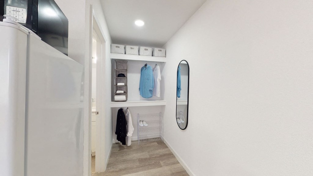 A white wall with a mirror and a shelf with clothes hanging on it.