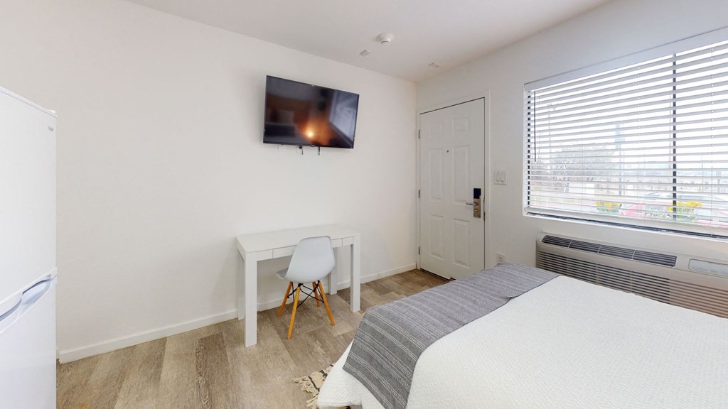 A bedroom with a bed, desk, chair, and a television mounted on the wall.