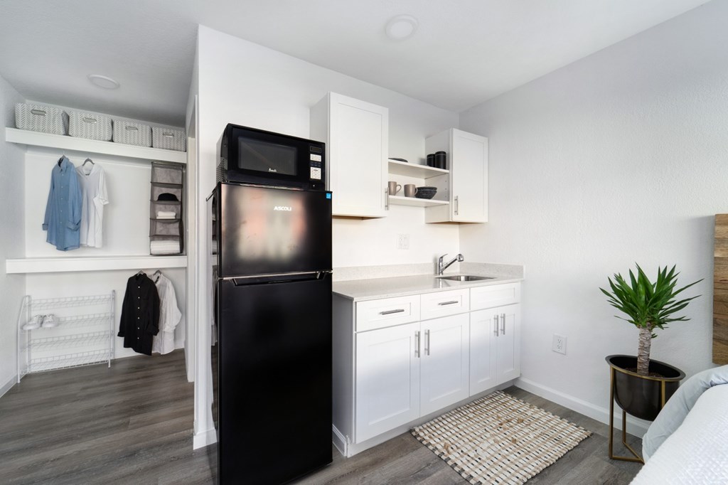 A black fridge in a kitchen with white cabinets and a white wall.