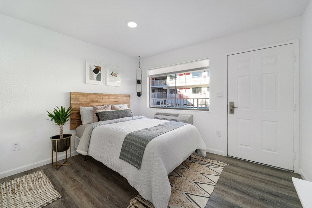 A bedroom with a bed, nightstand, and a window overlooking a street.
