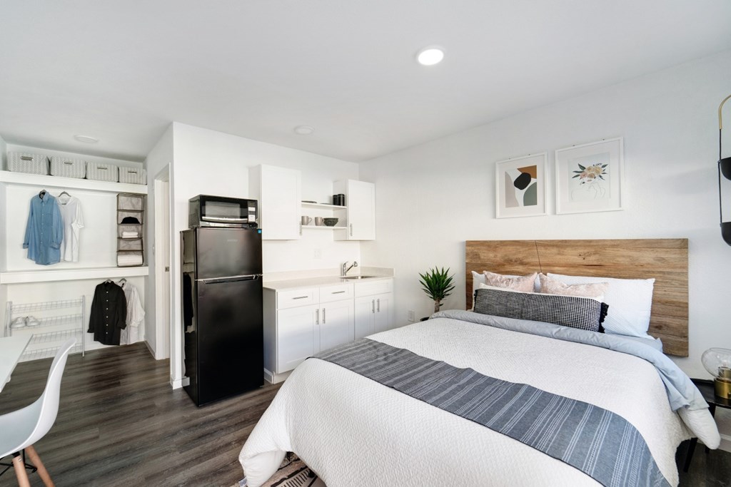 A bedroom with a bed, a chair, and a fridge.