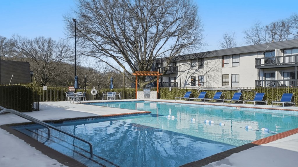 A swimming pool in front of a building with a tree in the background.