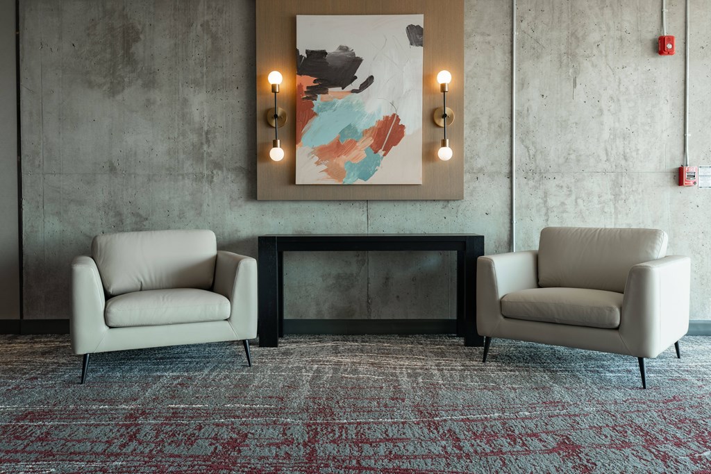 Two chairs and a table are in front of a wall with a painting and lights.