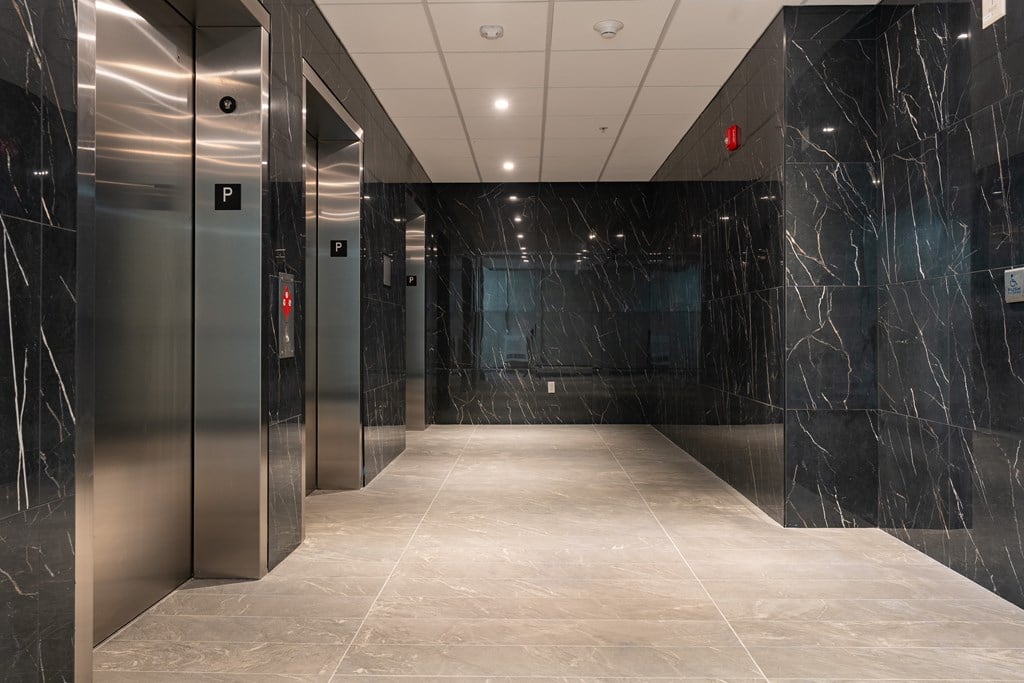 A long hallway with marble floors and walls and elevators on the side.