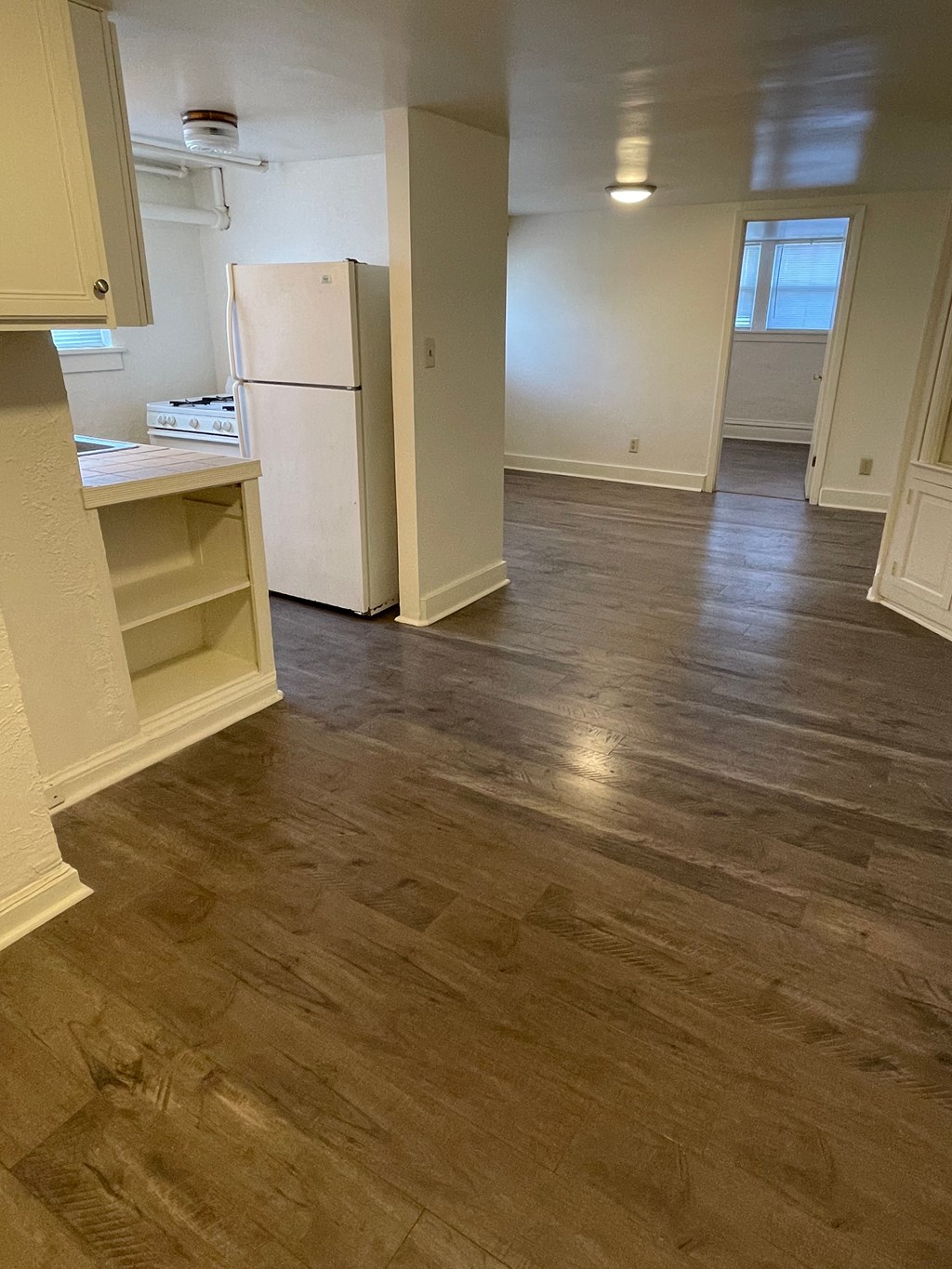 A kitchen with a white fridge and wooden floors.