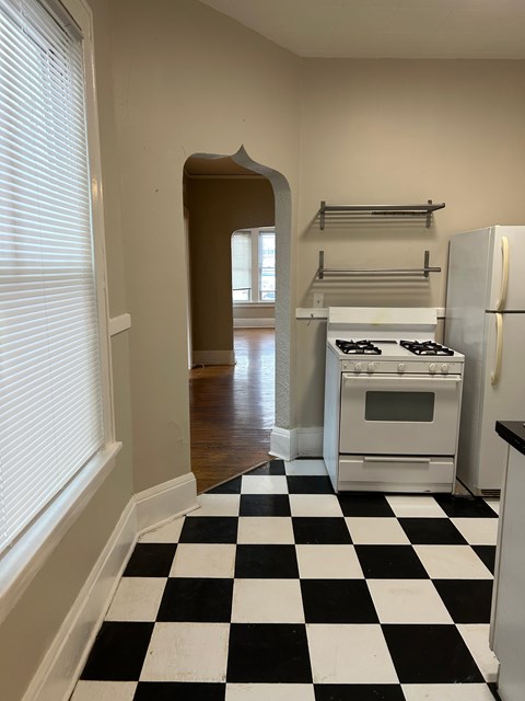 A black and white checkered floor leads to a kitchen with a white stove and refrigerator.