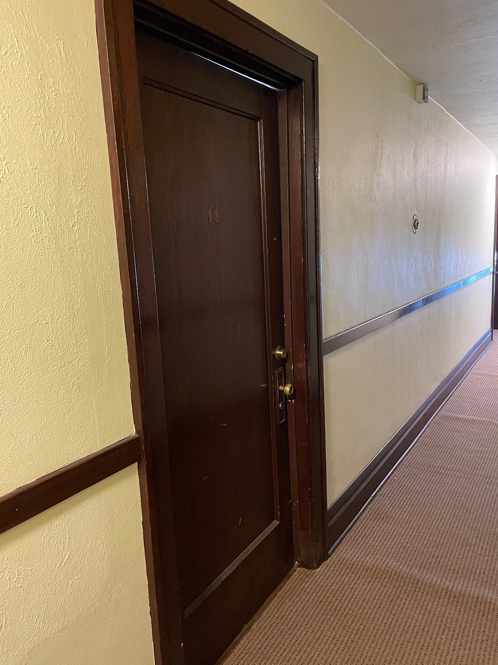 A brown door is open in a white hallway.