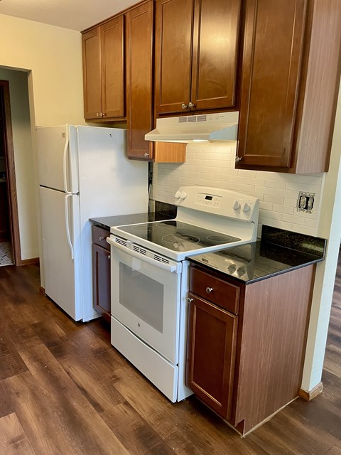 A white refrigerator and stove top oven in a kitchen with wooden cabinets.