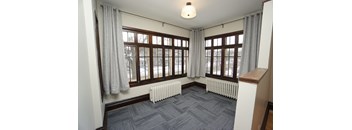 A room with a grey carpet and a window with curtains.