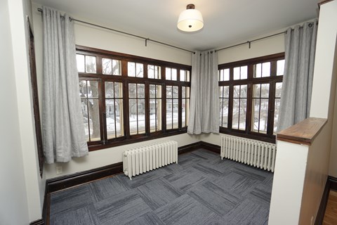 A room with a grey carpet and a window with curtains.
