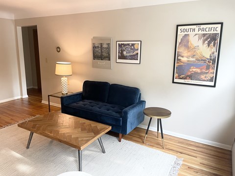 A living room with a blue couch, a wooden coffee table, and a poster on the wall.