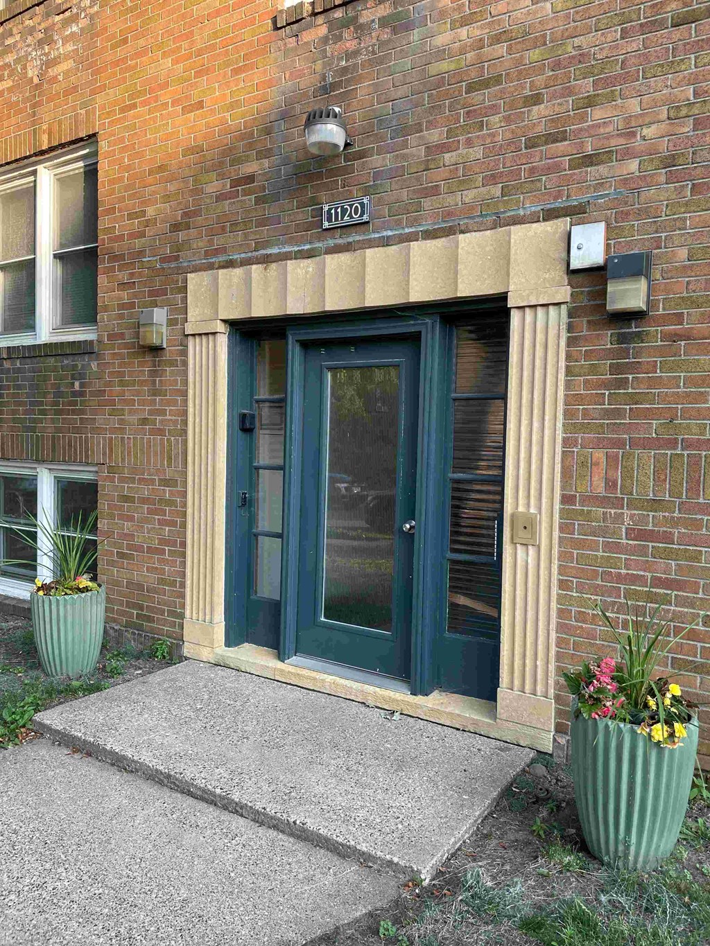 A green door is on a brick building with a number 1120 on the wall above it.
