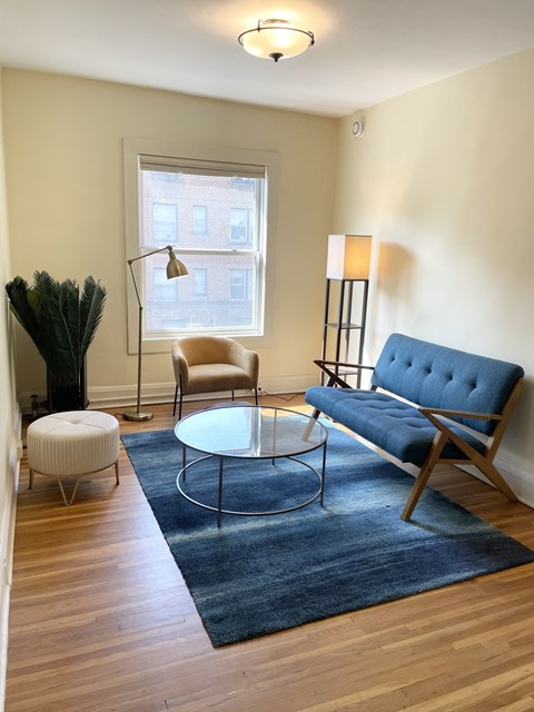 A blue sofa sits in a living room with a glass table in front of it.