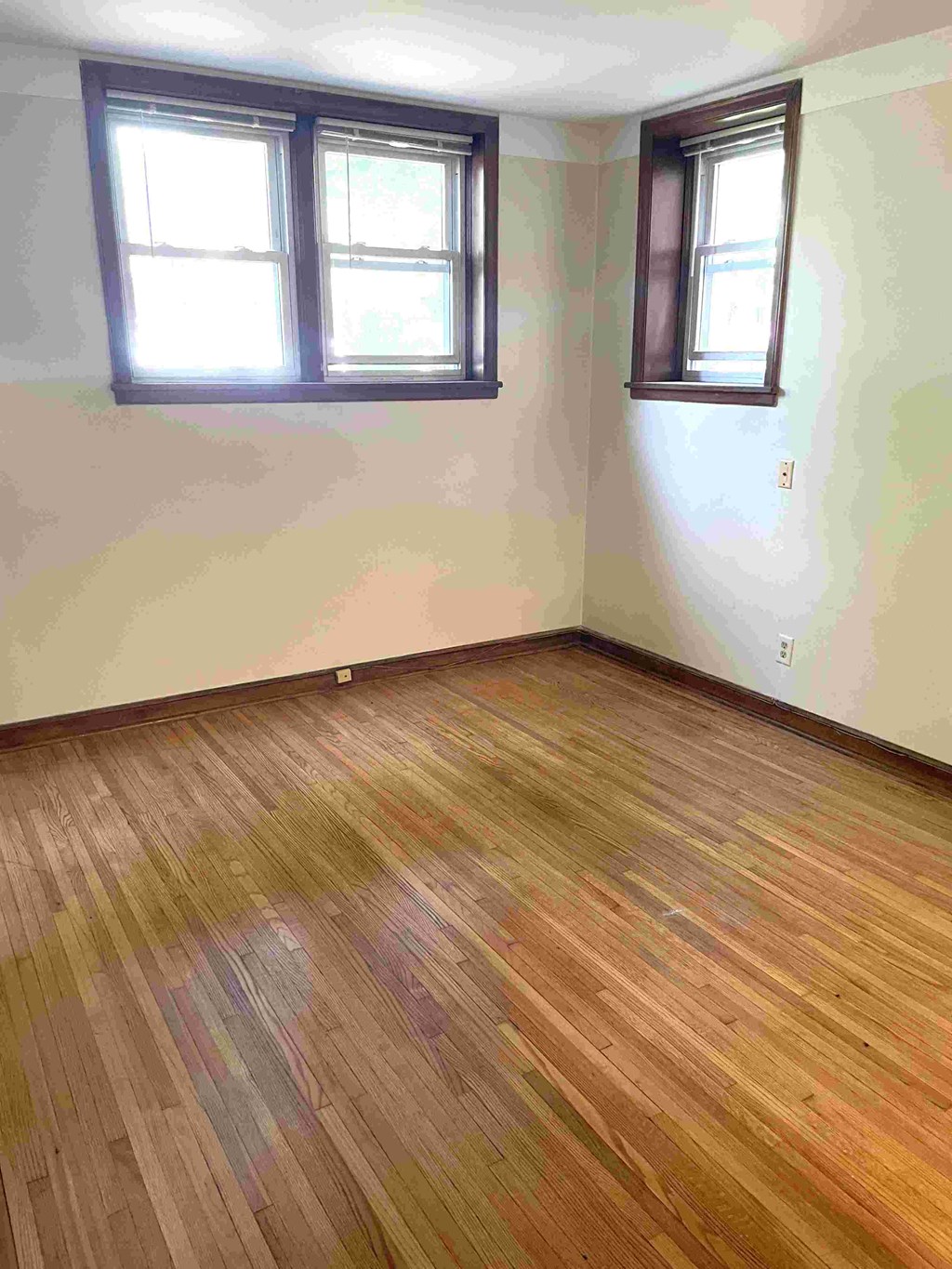 A room with wooden flooring and two windows.