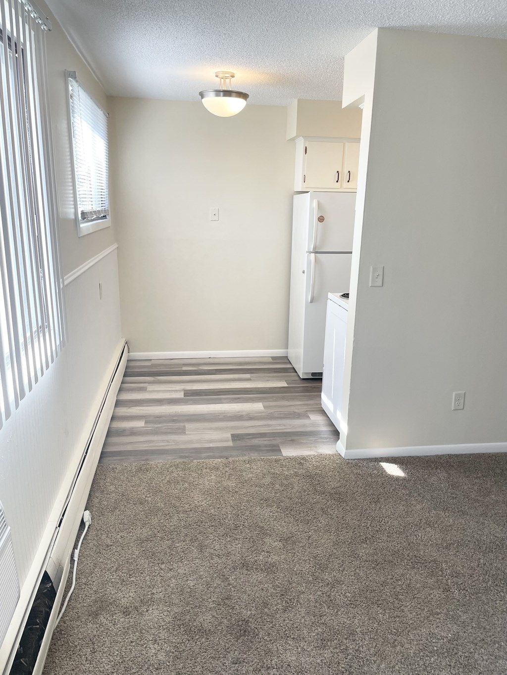 A room with a carpeted floor and a white refrigerator.
