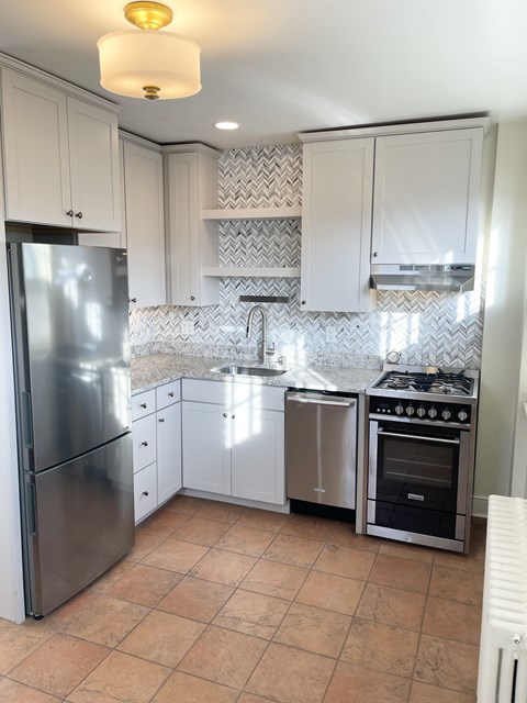 Professionally designed kitchen with custom cabinetry, granite countertops, attractively tiled backsplash and stainless steel appliances, including dishwasher and range hood.