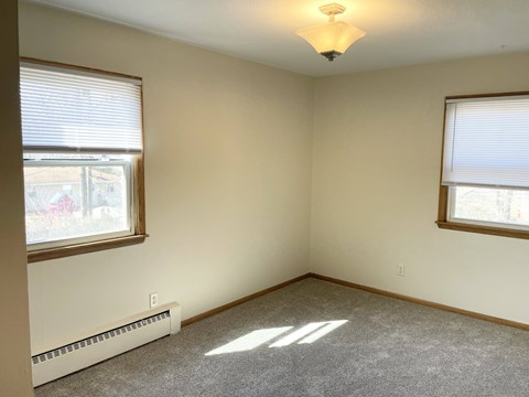 A room with a carpeted floor, a window with blinds, and a ceiling fan.