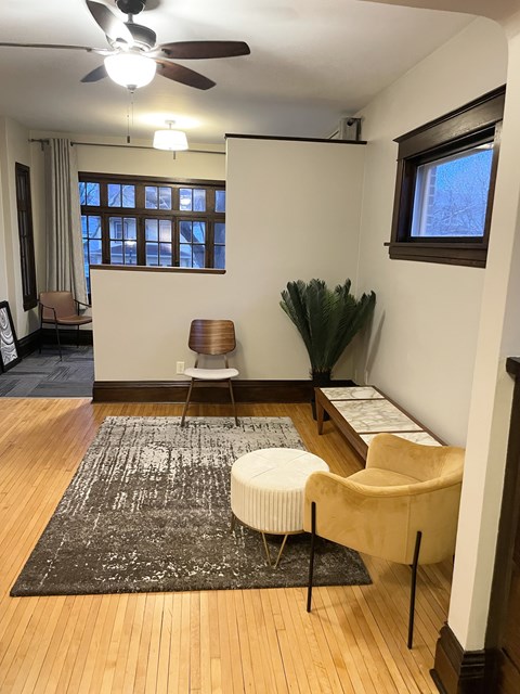 A room with a fan, a chair, a table and a plant.