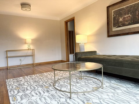 A living room with a glass table and a grey sofa.