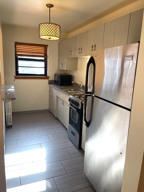 A kitchen with a stainless steel refrigerator and a window with blinds.