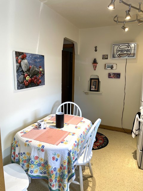 A dining room with a floral tablecloth and a painting of rocks on the wall.